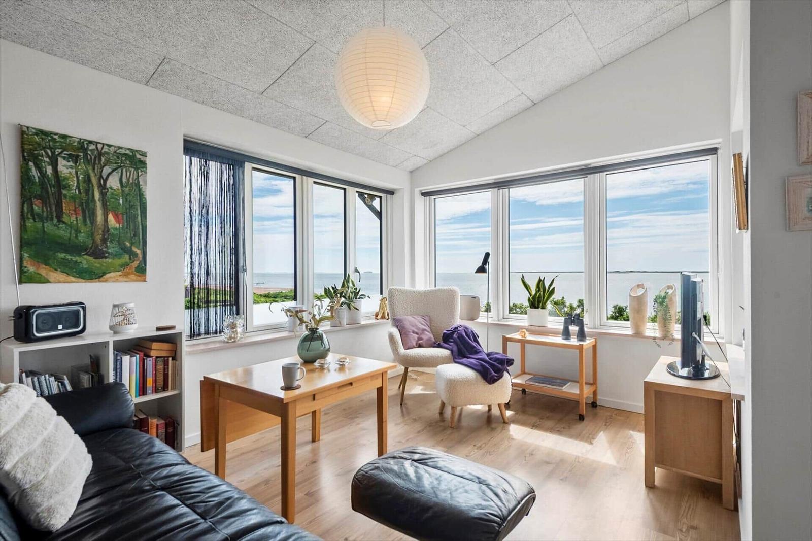 Wohnzimmer mit Blick aufs Meer, Holzmöbel und großflächigen Fenstern.