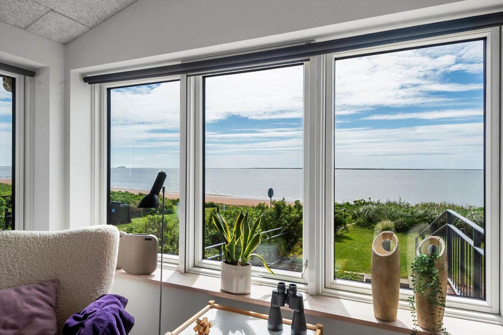 Großes Fenster mit Meerblick, Pflanzen und Fernglas auf Fensterbank.