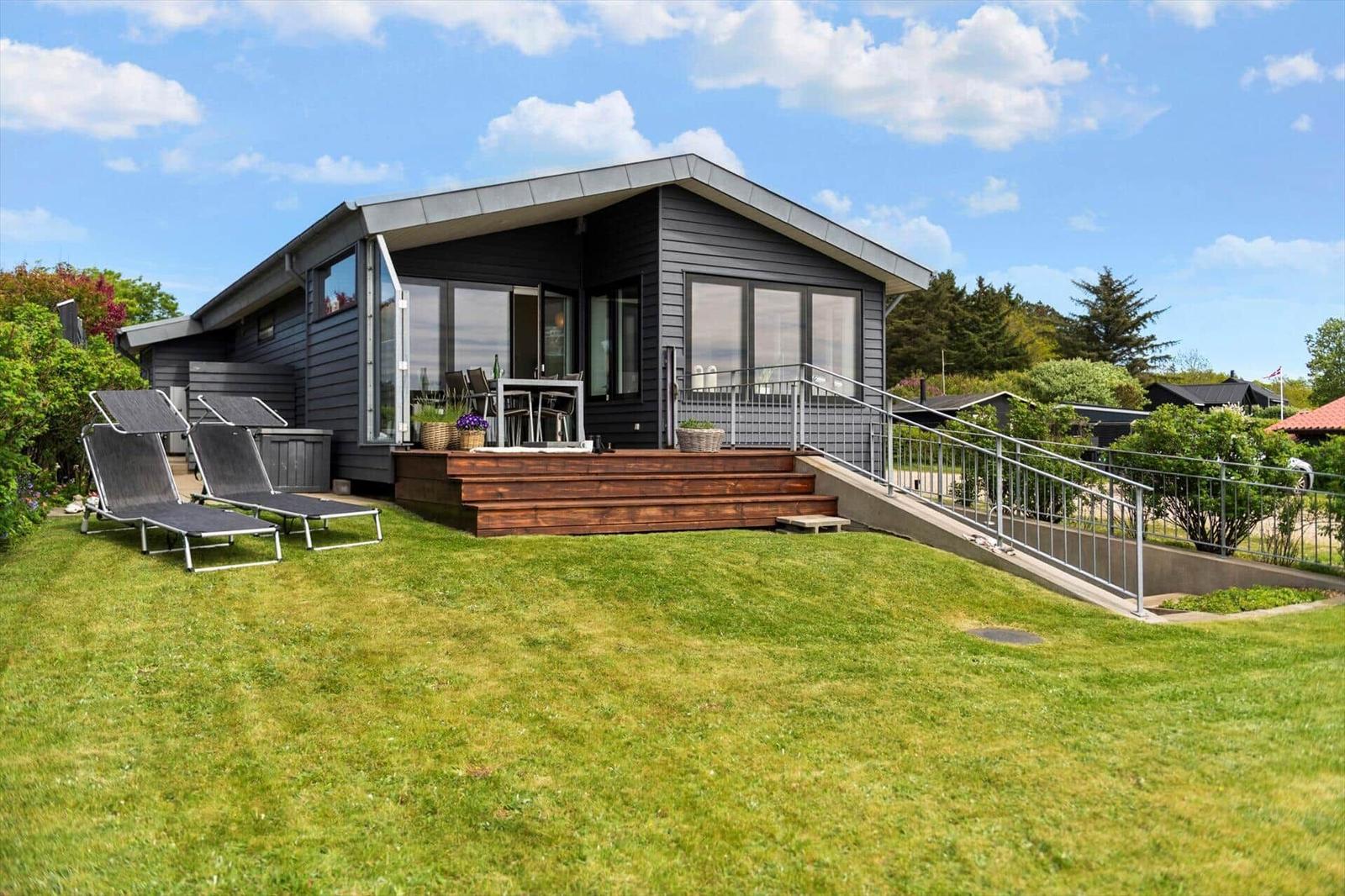 Moderne Ferienhaus mit Terrasse, Liegestühlen und Grünfläche. Zugang über Rollstuhlrampe.