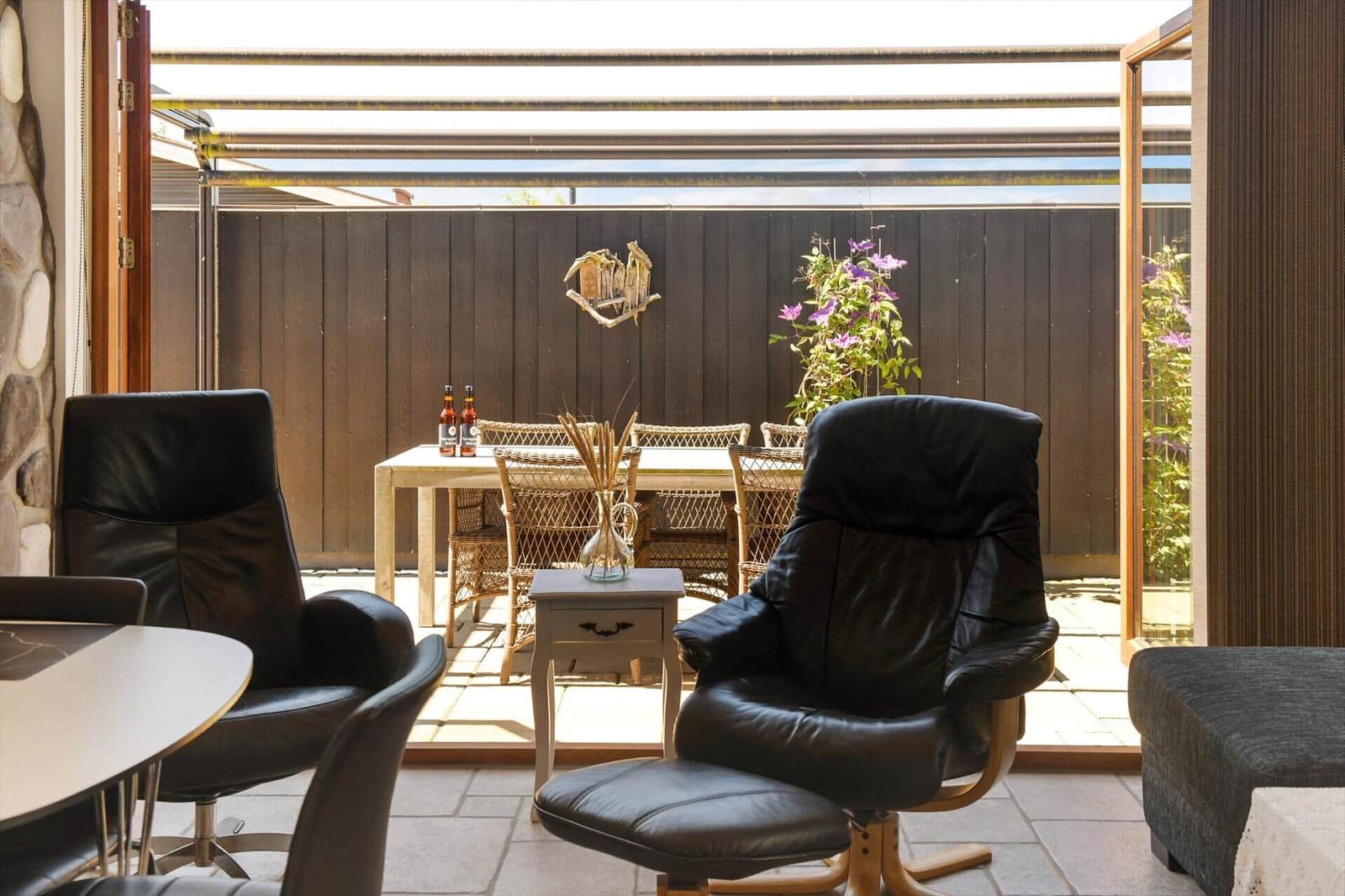 Terrace with seating and table. Background: wooden fence and plants.