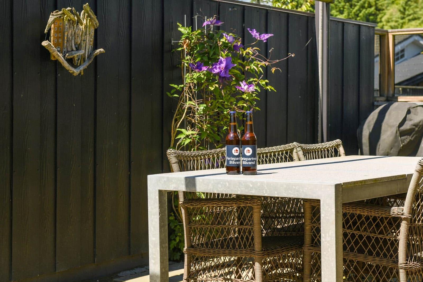 Backyard with table, chairs, and two beer bottles. Plant with purple flowers on the wall.
