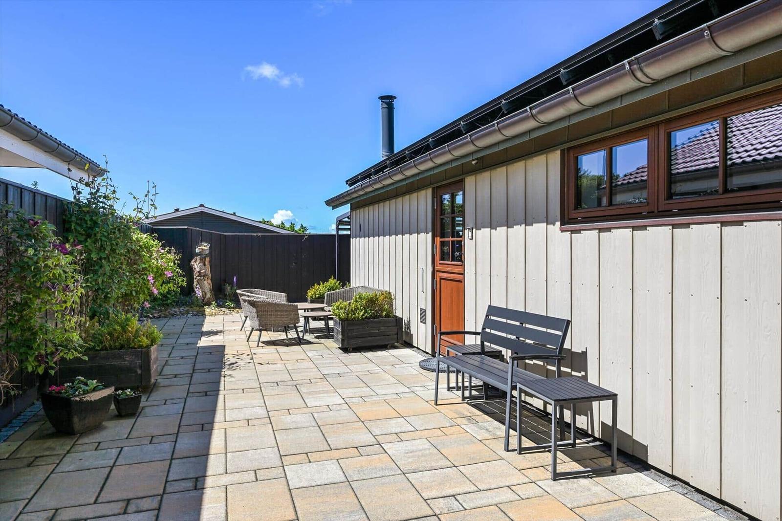 Terrace with seating and plants in front of a house with wooden siding.
