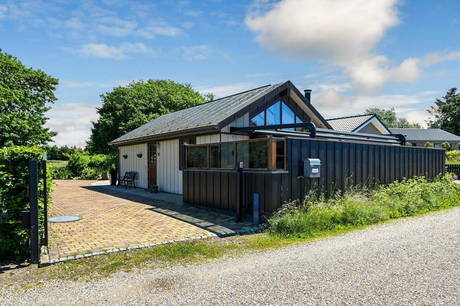 Modern villa with wooden siding, large windows, and paved courtyard under blue sky.