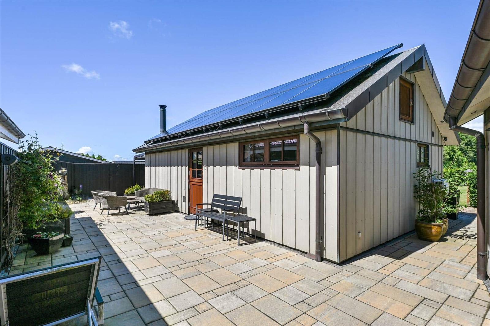 House with solar panels, terrace, and garden furniture under blue sky.