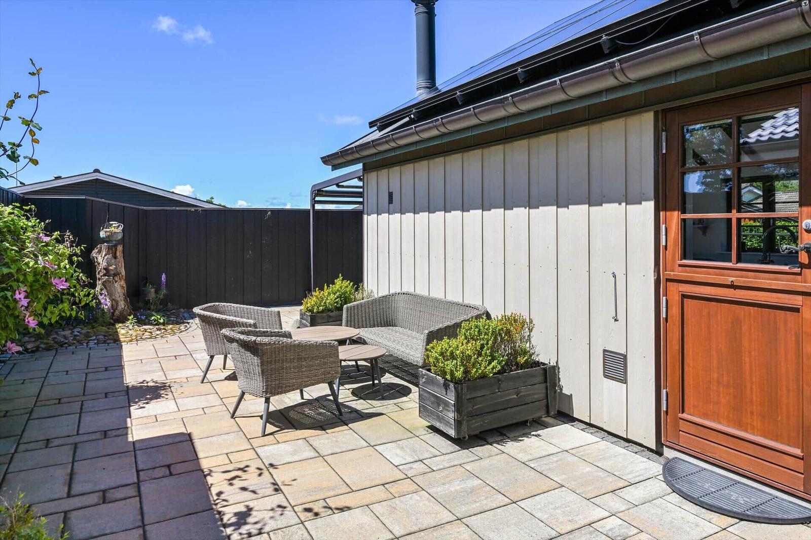 Terrace with seating, plants, and wooden door. Backyard with fence and flowerbed.