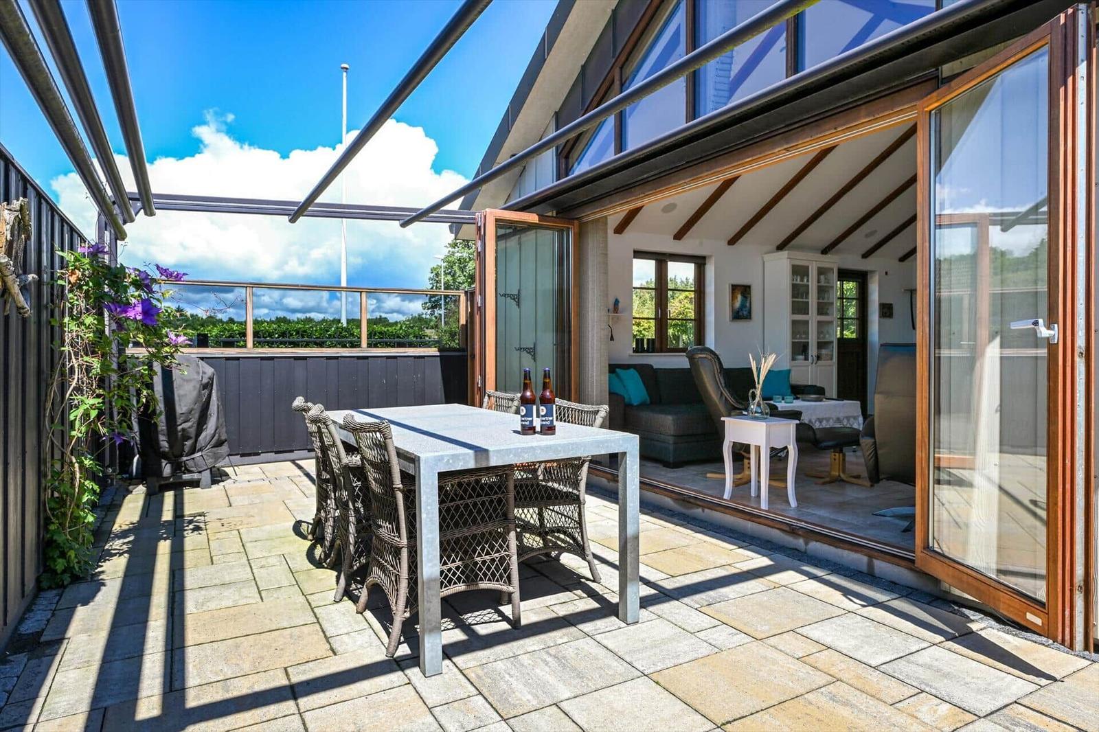 Terrace with table and chairs. Living room visible through glass doors.