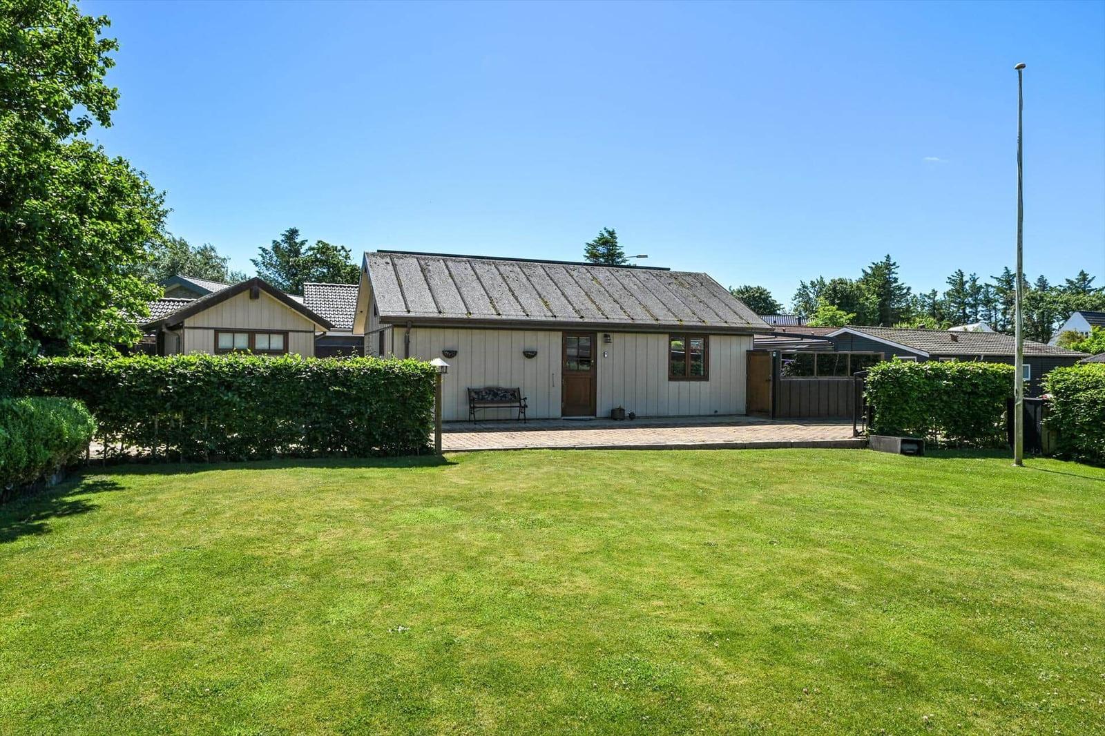 A vacation home with lawn, hedge fence, and wooden veranda under blue sky.
