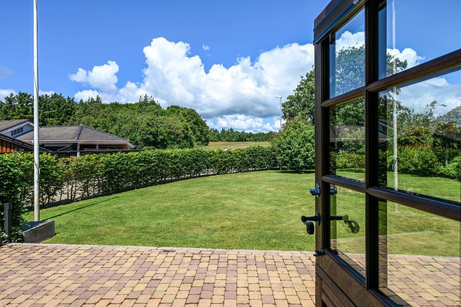 From the door, you see a green lawn with hedge and trees under blue sky.