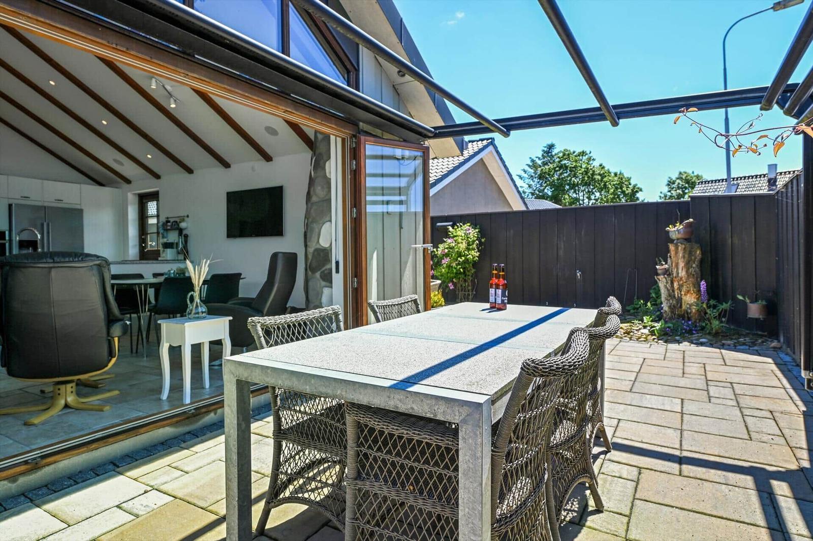 Terrace with table and chairs, view into house with kitchen and living area.