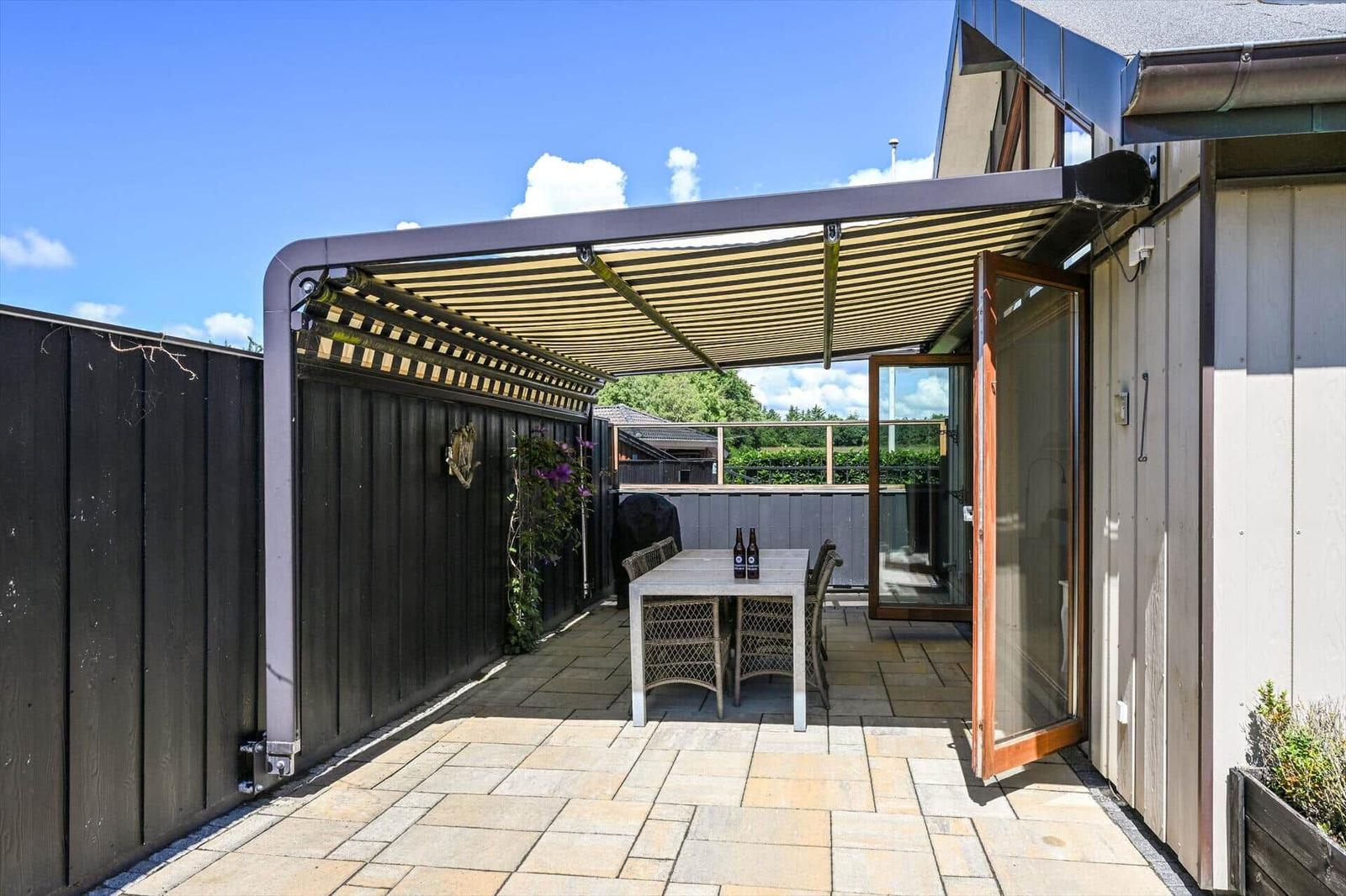 Terrace with awning, table and chairs. Backyard with wooden railing and garden.