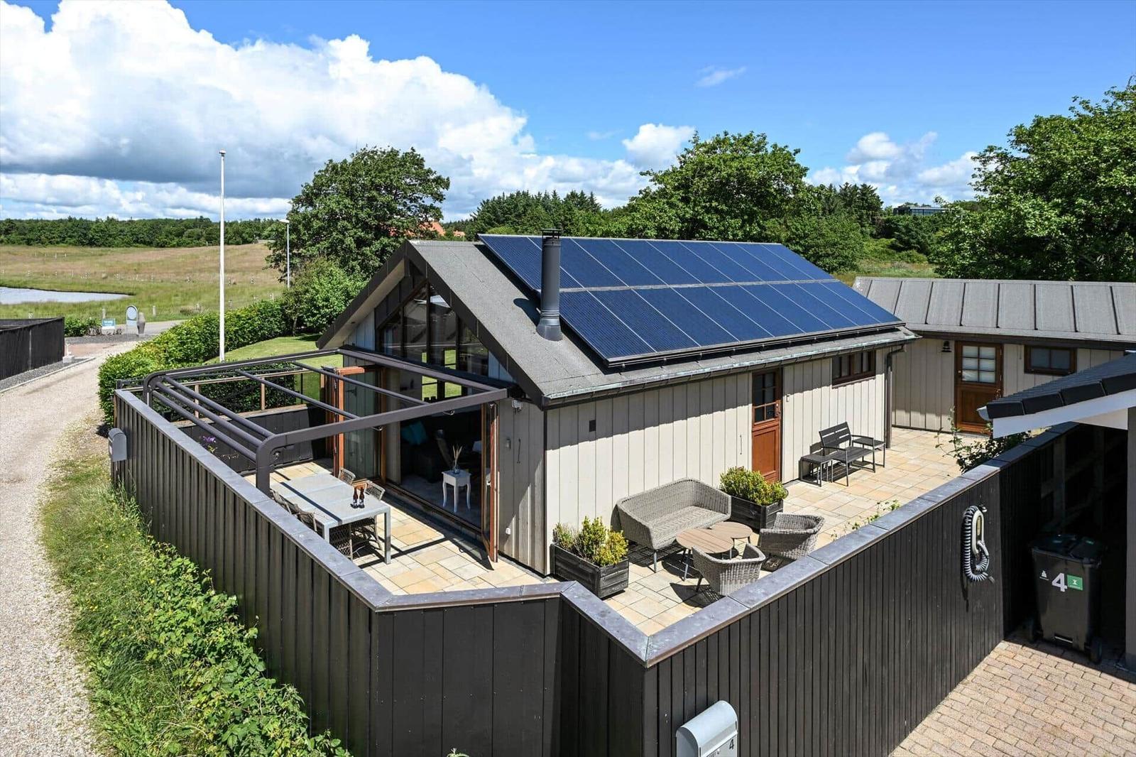 Modern villa with solar panels and terrace. Garden area with seating.