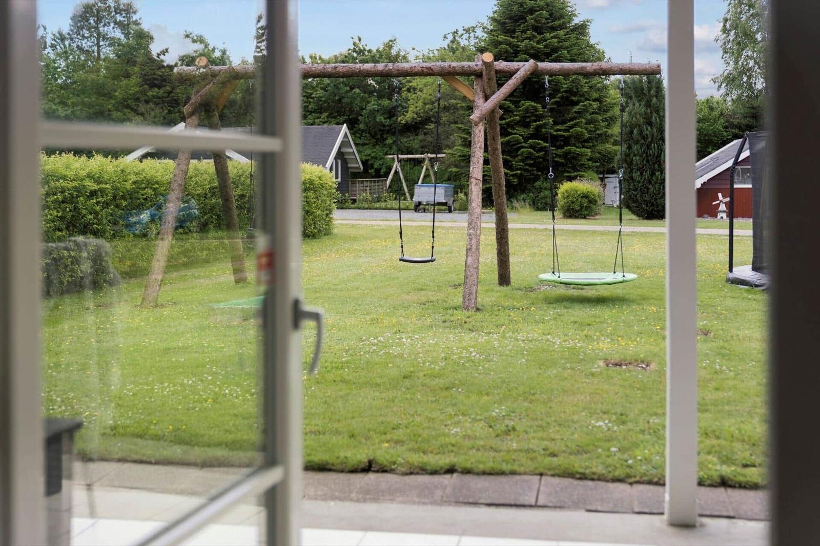 View from inside: Playground with swing and trampoline in the garden.