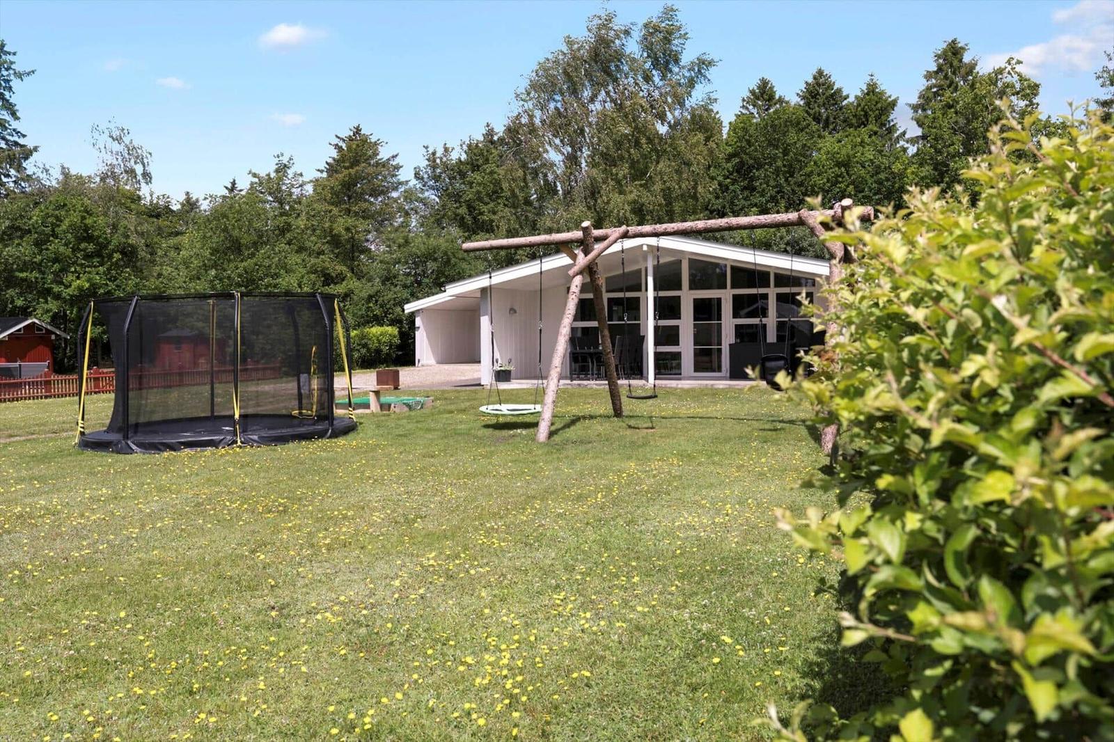 A house with a large garden, swing, and trampoline. Surrounded by trees and grass.
