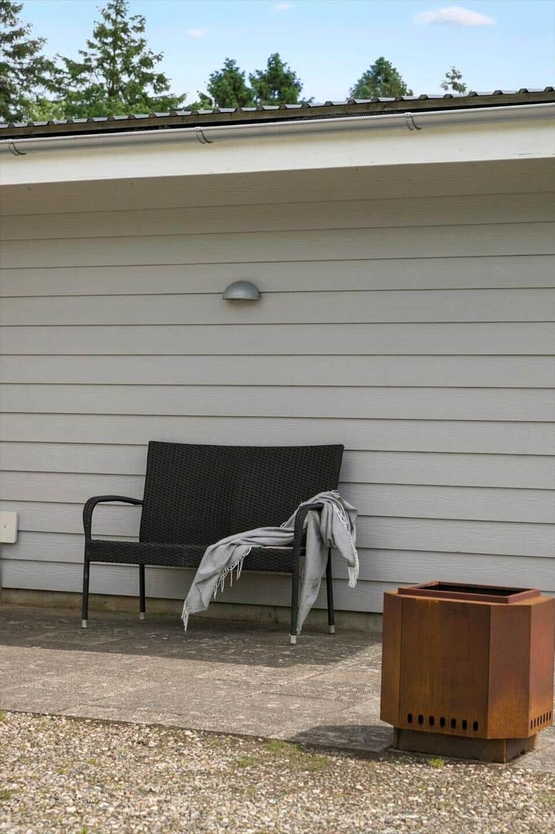 A bench with a blanket stands in front of a house. Beside it is a fire pit.