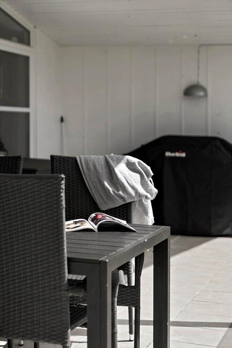 Terrace with table, chairs, and open magazine. Grill and wall light in background.