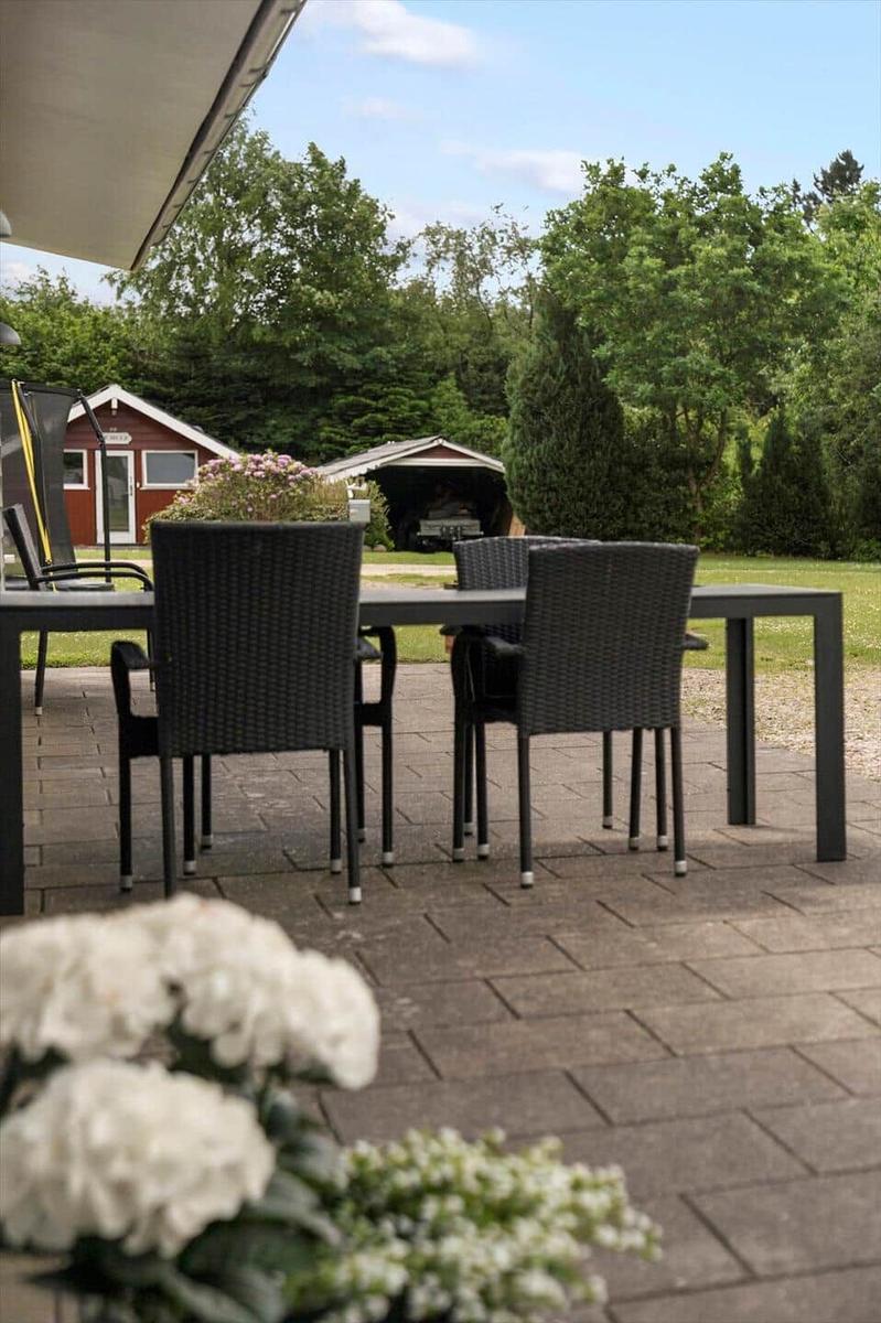 Patio with table and chairs, view of garden and red house.