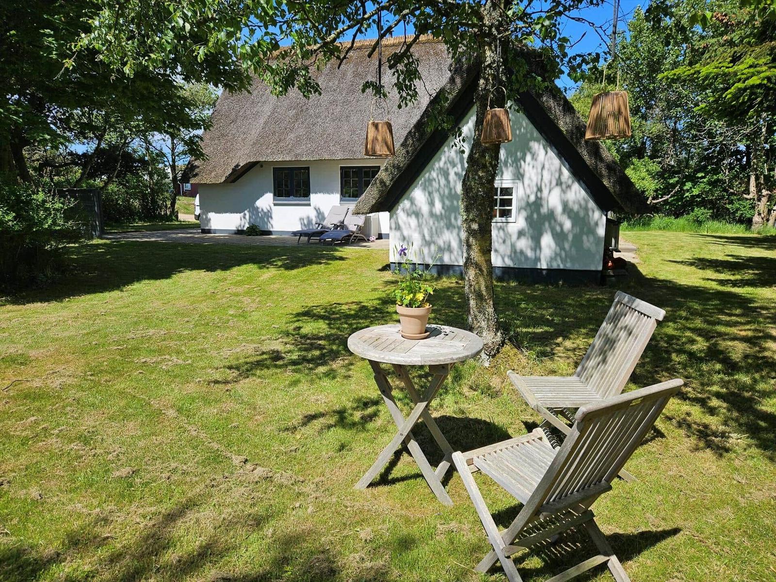 Haus mit Strohdach, Garten mit Tisch und Stühlen, Bäume und Hängelampen.