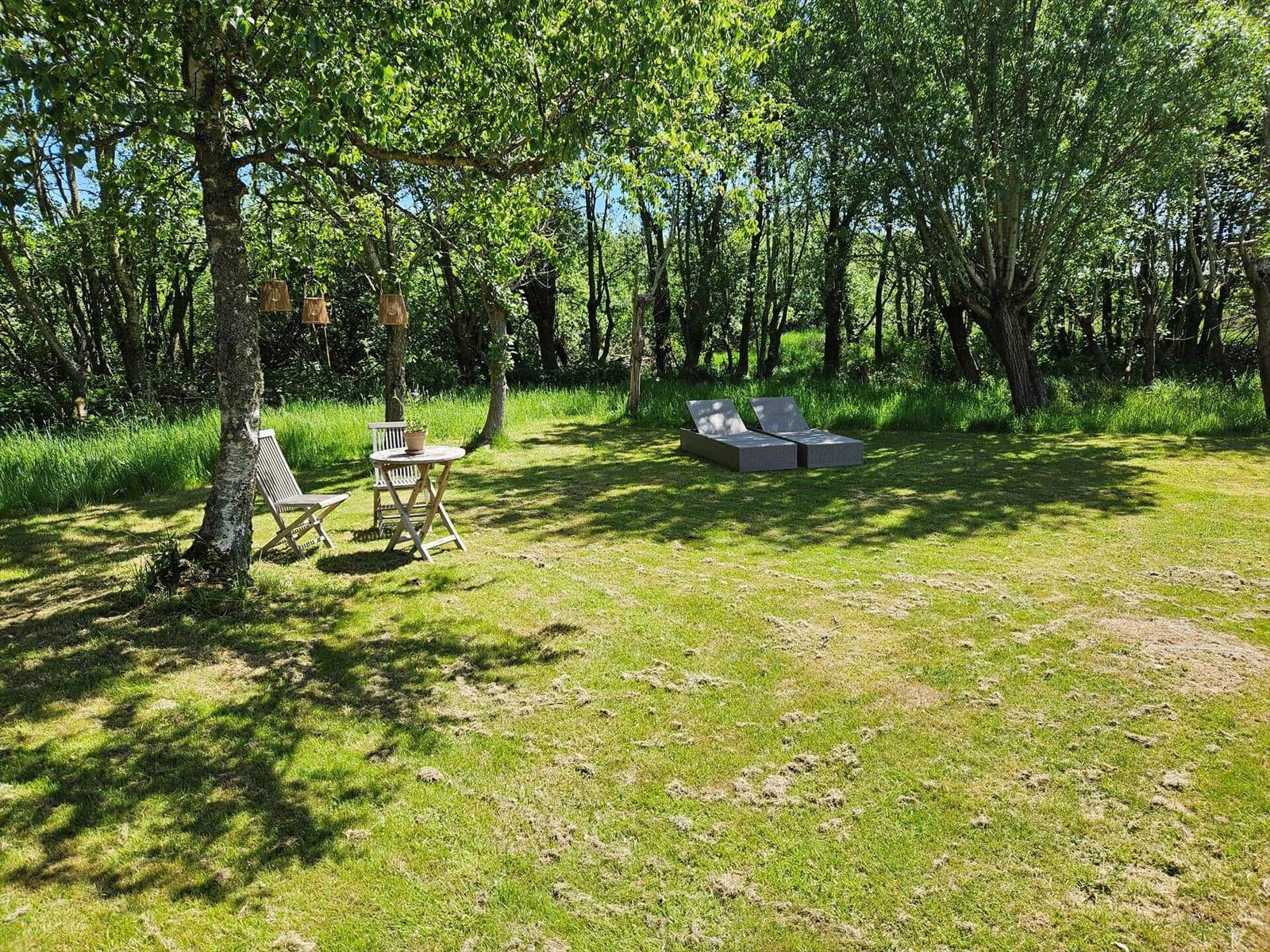 Grüner Garten mit Liegestühlen und Tisch unter Bäumen.