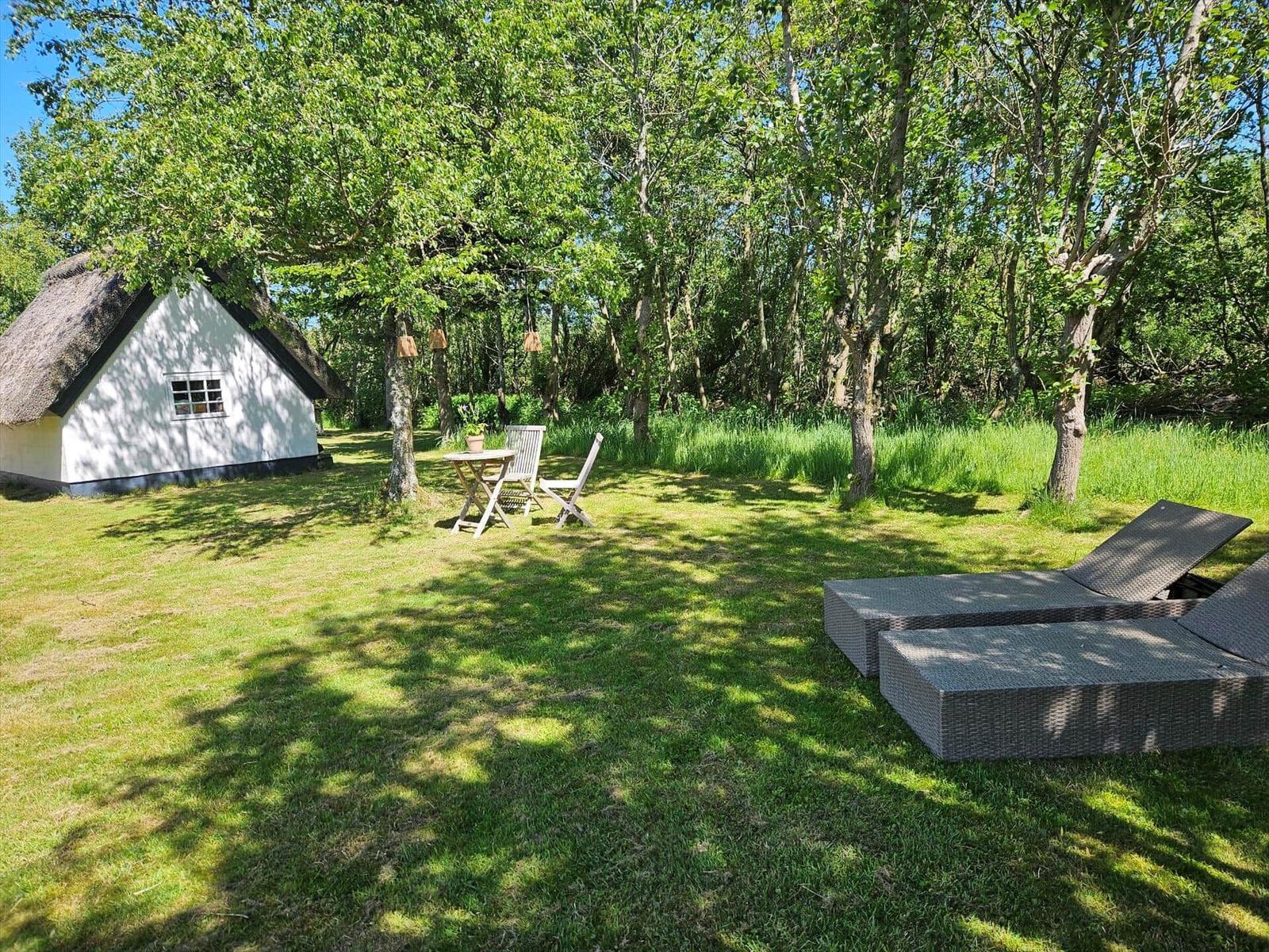 Hütte mit Dach aus Stroh, Garten mit Liegen und Tisch unter Bäumen.