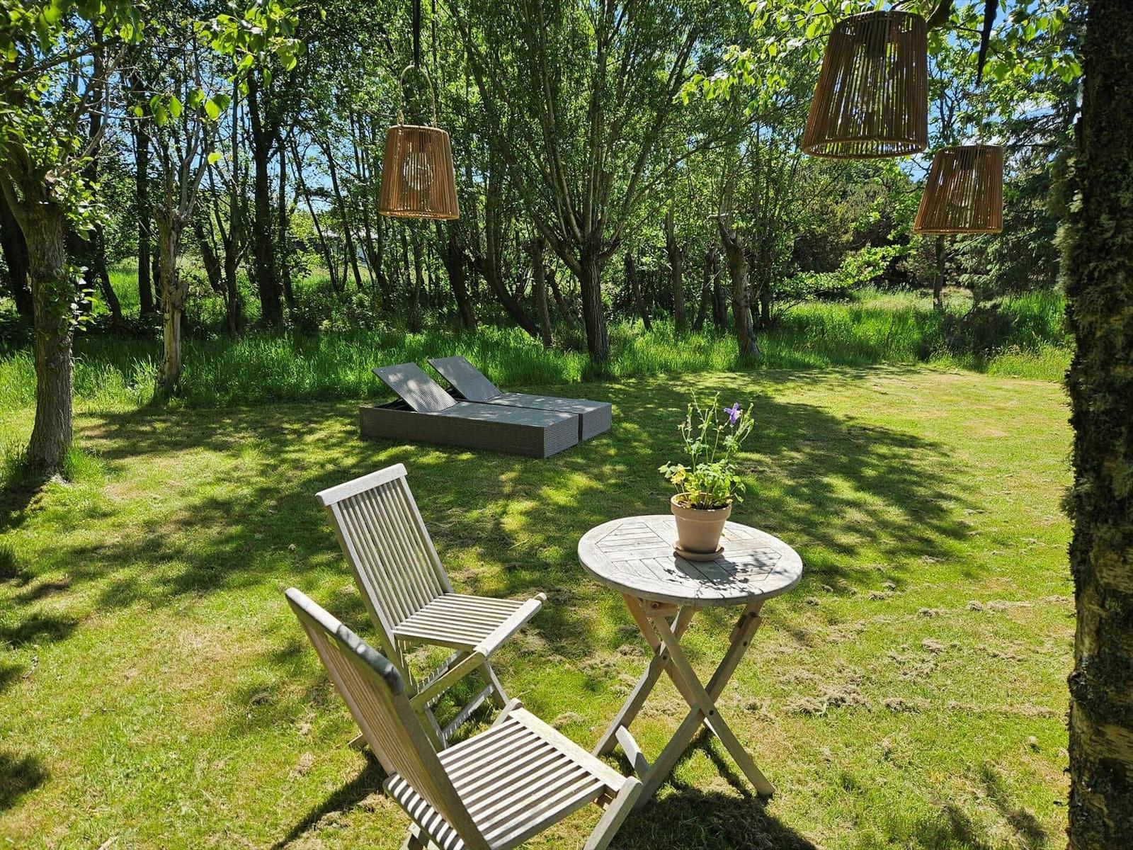 Garten mit Liege, Tisch und Stühlen unter Bäumen mit hängenden Lampen.
