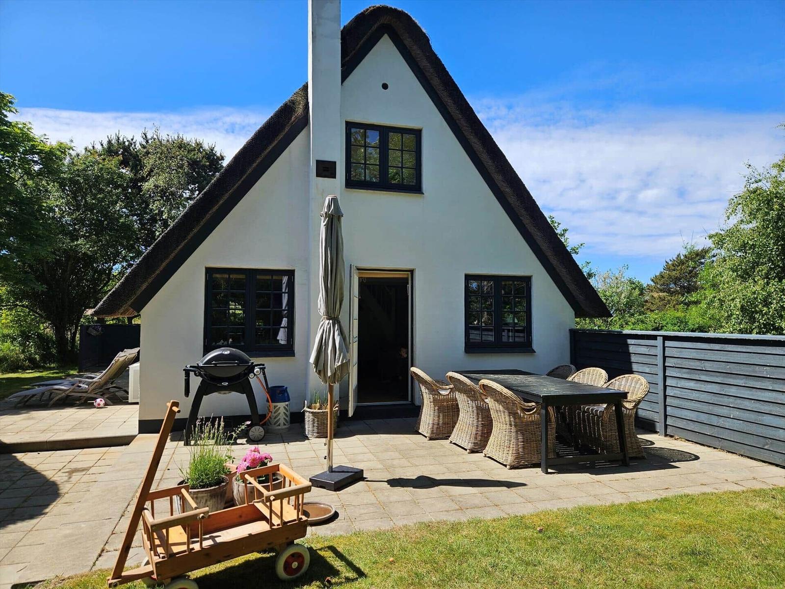 Wohnhaus mit Dach, Terrasse, Grill und Sitzgruppe im Freien.