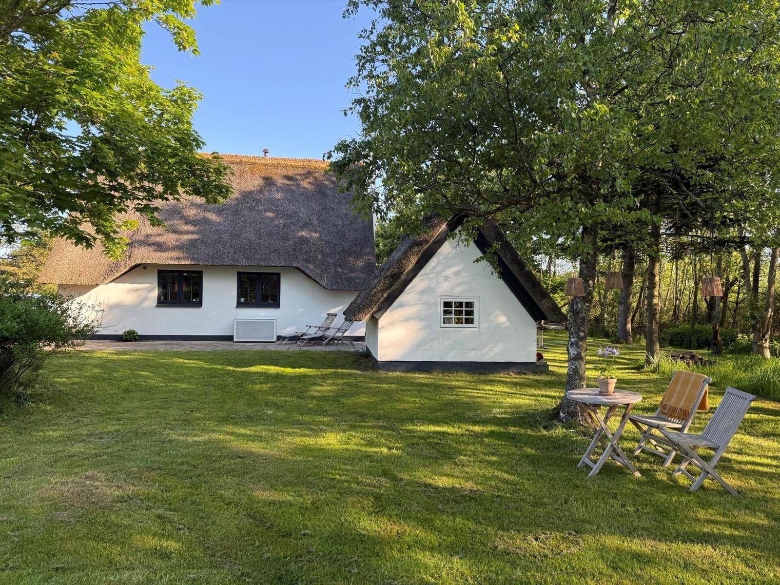 Haus mit Strohdach, Gartenbereich mit Tisch und Stühlen unter Bäumen.