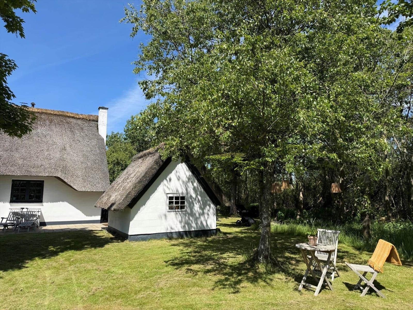 Haus mit Strohdach und Garten mit Tisch und Stühlen unter Bäumen.