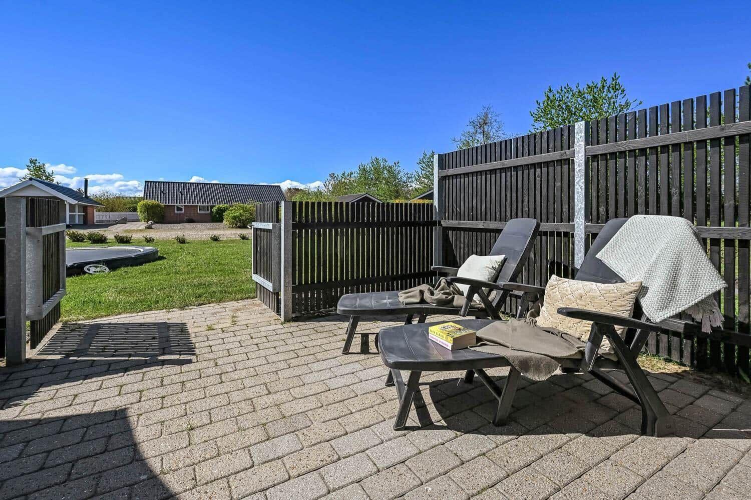 Terrasse mit zwei Liegestühlen und Tisch. Hinterhof mit Zaun und Grünfläche.