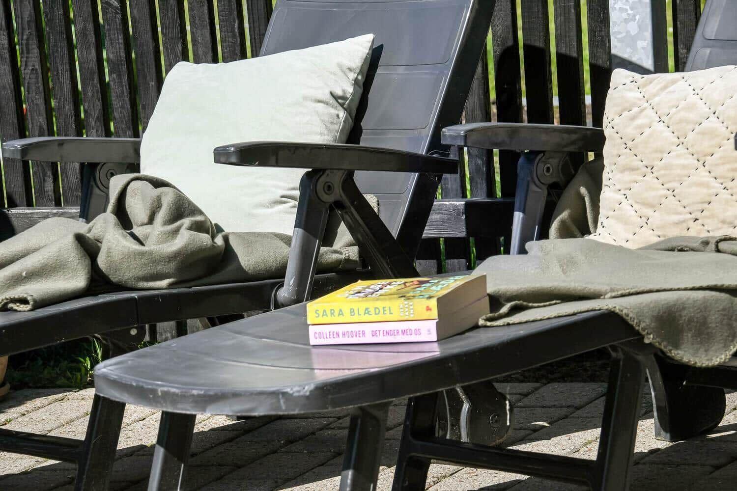 Zwei Liegestühle mit Kissen und Decken. Auf dem Tisch liegen zwei Bücher.