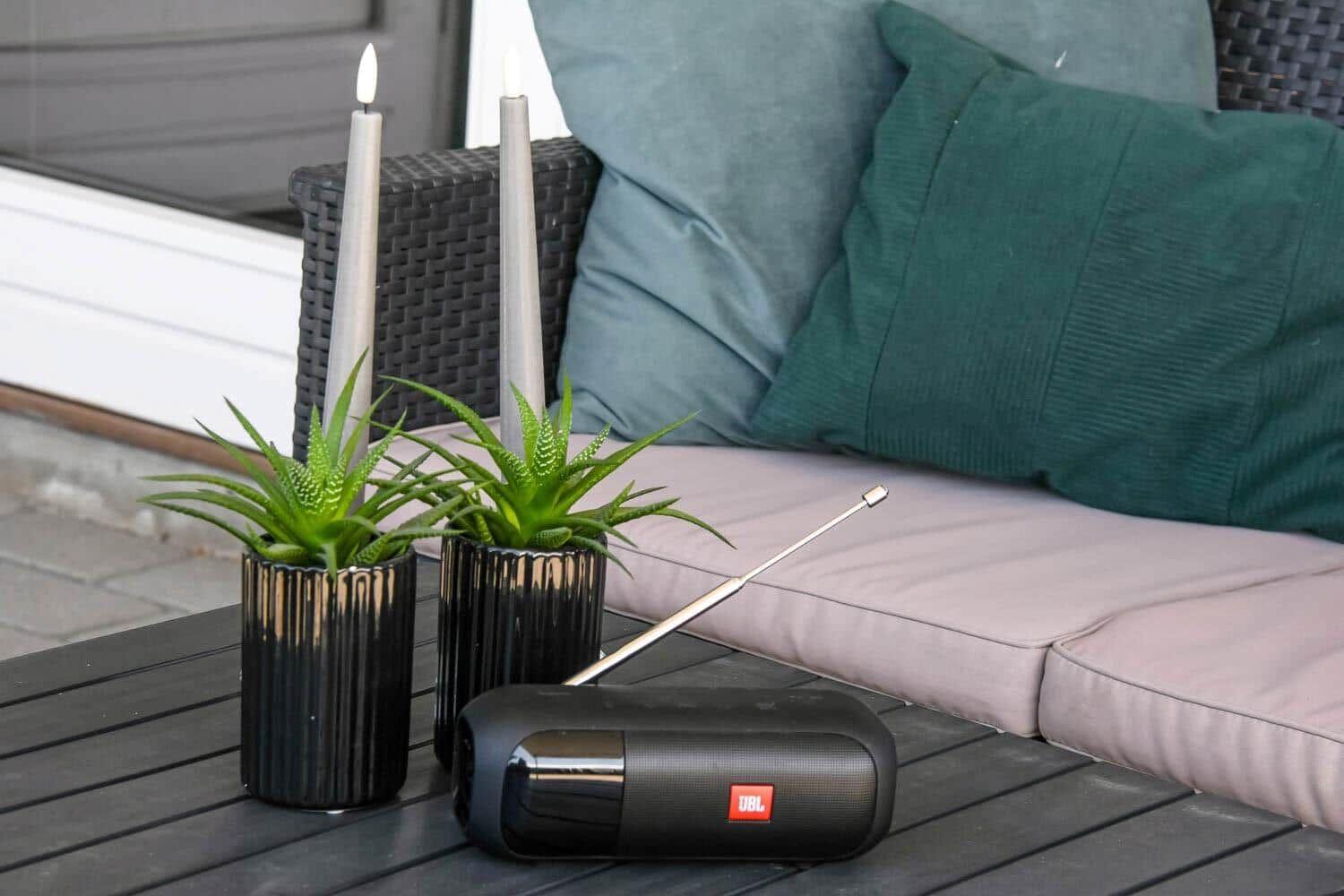 Auf der Terrasse stehen zwei Pflanzen, Kerzen und ein Lautsprecher auf einem Tisch.