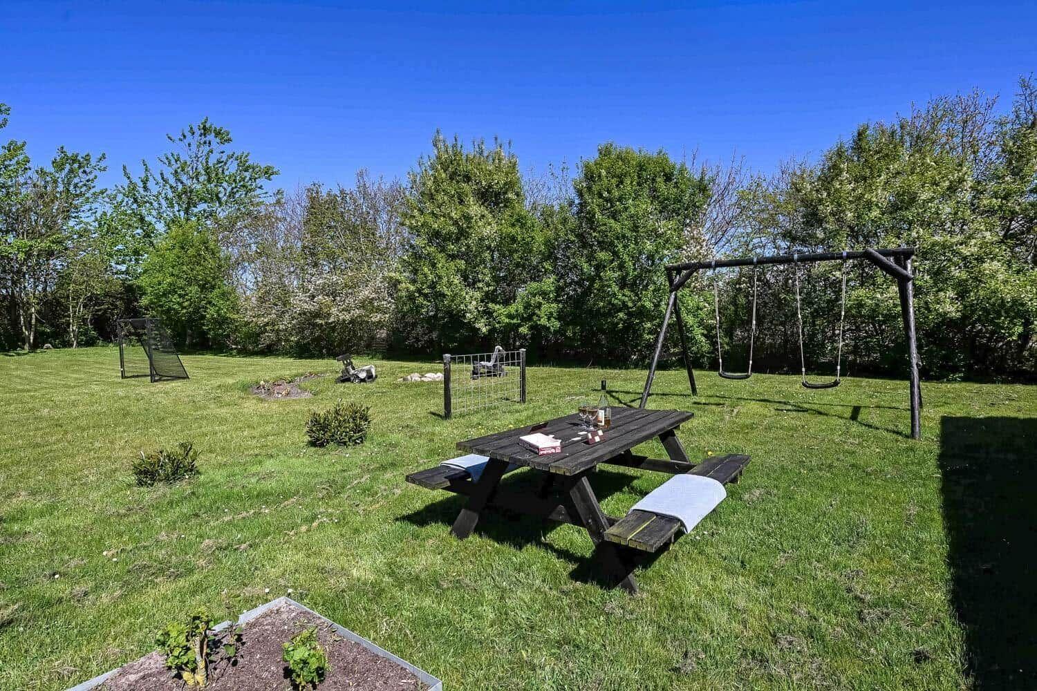 Hinterhof mit Picknicktisch, Schaukel und Spielplatz im Gras.