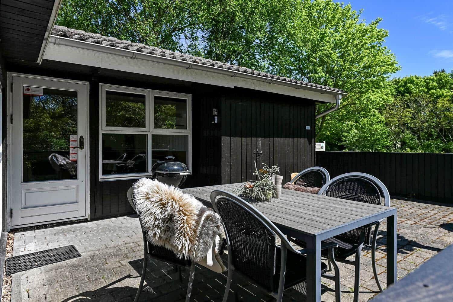 Terrasse mit Tisch, Stühlen und Grill vor einem Haus mit dunkler Fassade.