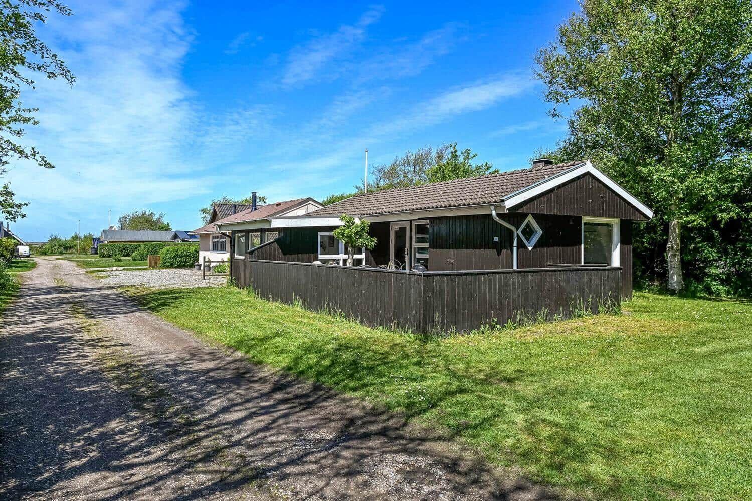 Holzhaus mit Garten und Zaun unter blauem Himmel