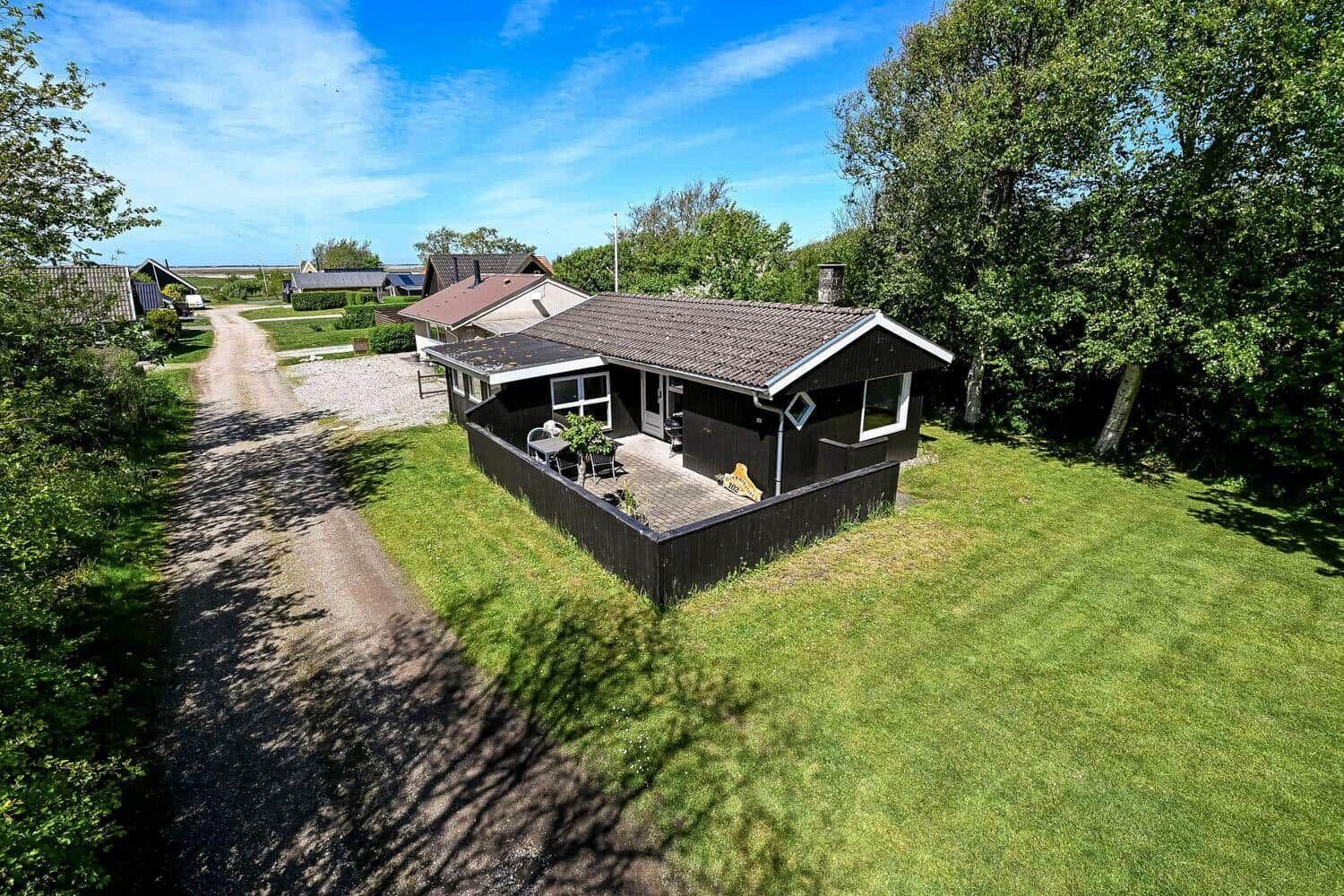 Schwarzes Haus mit Terrasse, umgeben von Gras und Bäumen unter blauem Himmel.