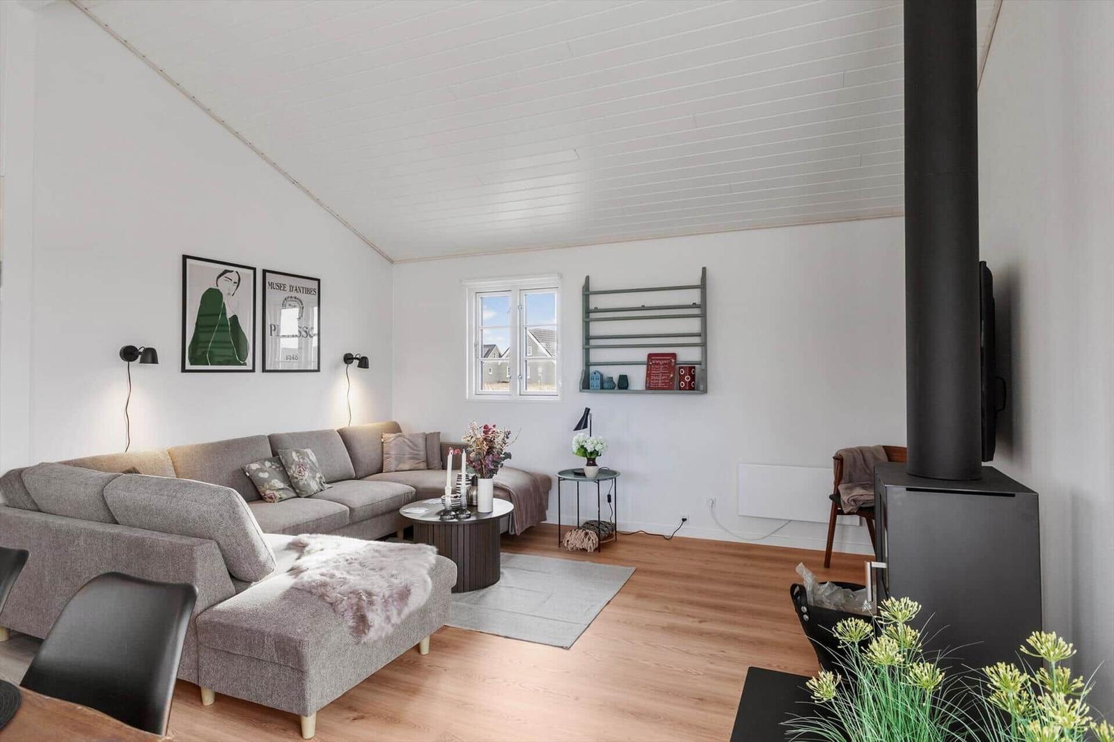 Wohnzimmer mit Sofa, Kamin und Fenster. Holzboden und weiße Wände.