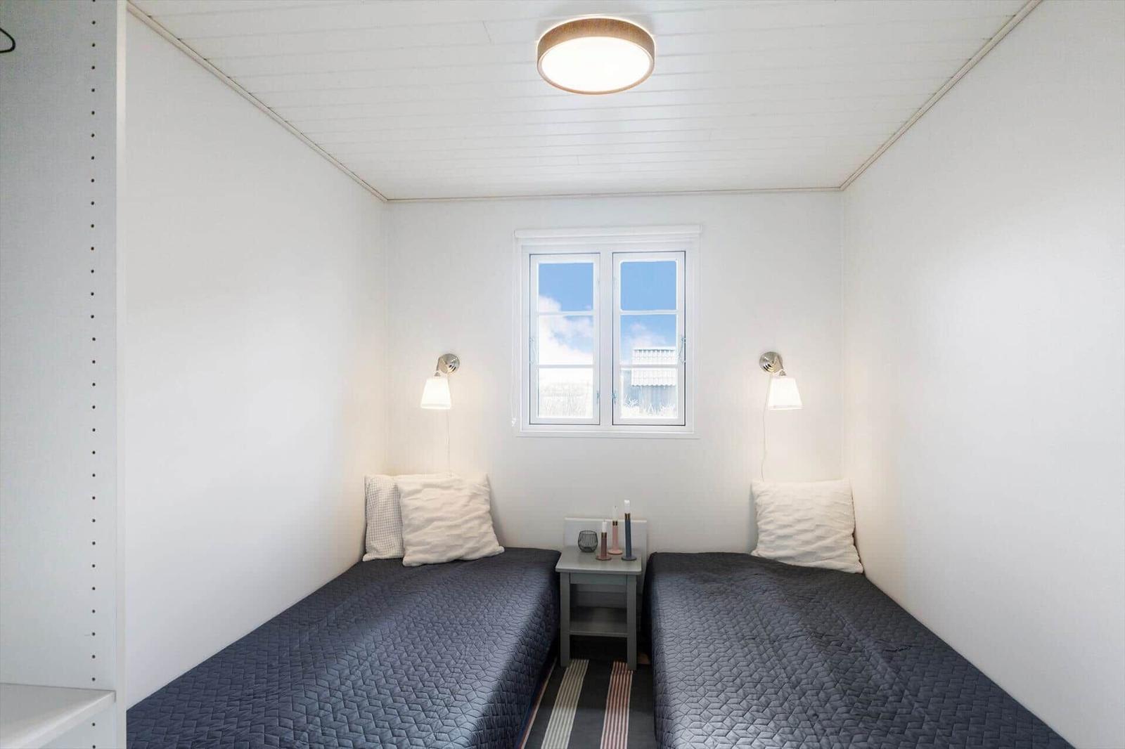 Zwei Betten mit dunklen Bezügen stehen gegenüber einem Fenster mit weißen Rahmen.