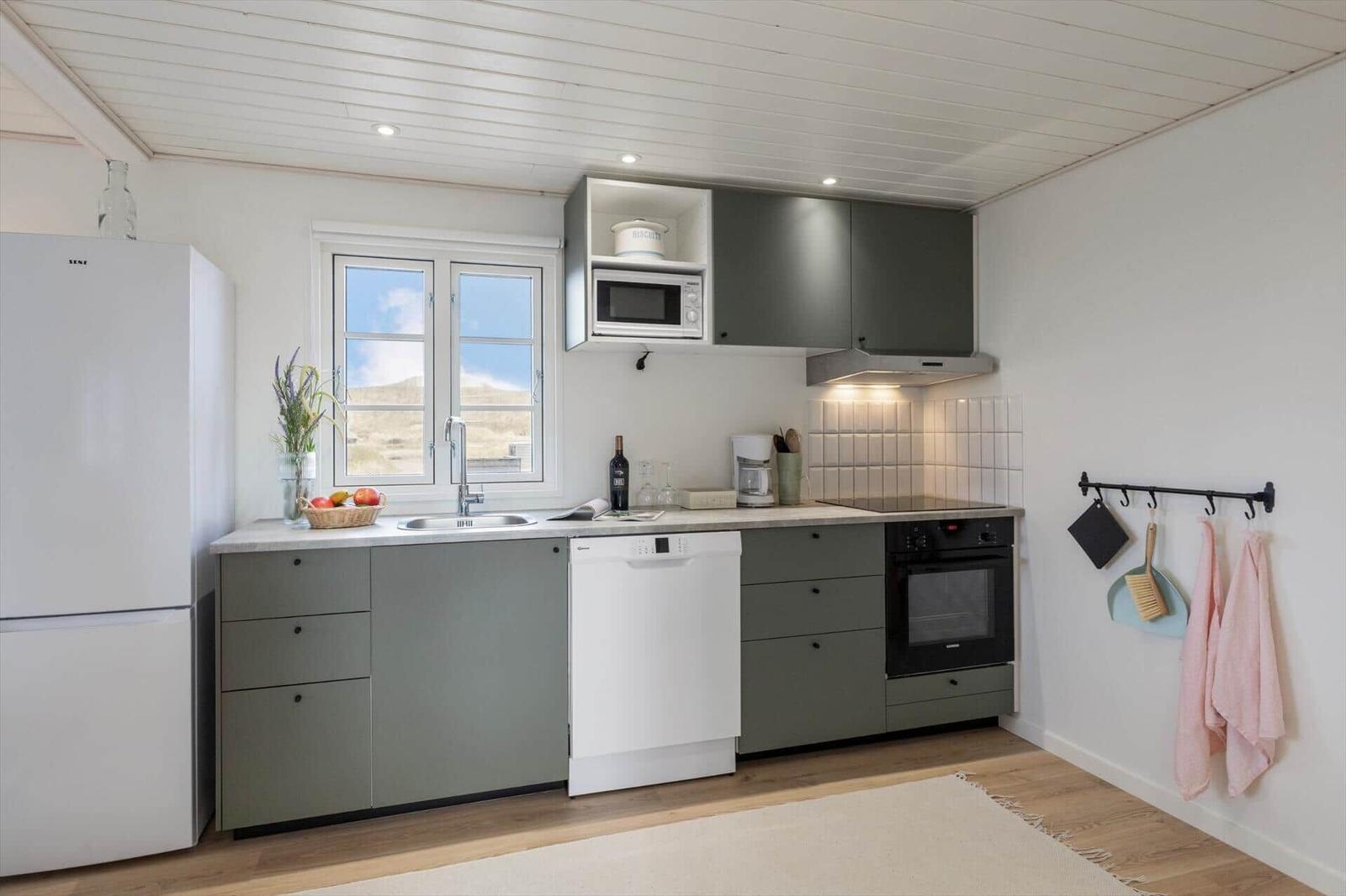Küche mit grauen Schränken, weißem Kühlschrank und Fenster mit Blick.
