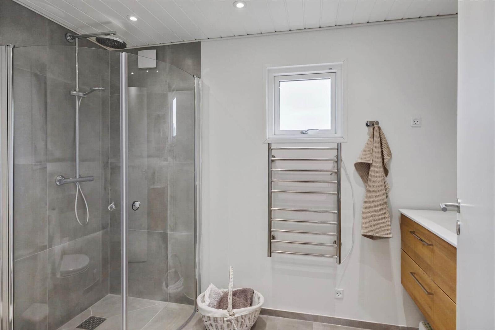 Dusche mit Duschbrause, Fenster, Heizkörper und Waschbecken mit Schrank.