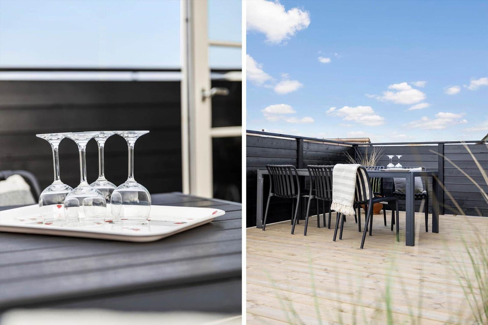 Terrasse mit Tisch, Stühlen und Weinflaschen. Holzdecke und schwarze Brüstung.