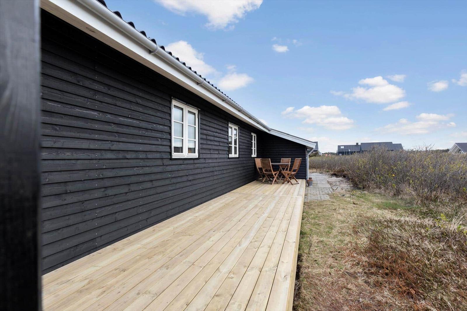 Schwarzes Holzhaus mit Terrasse und Garten. Tisch und Stühle auf der Terrasse.