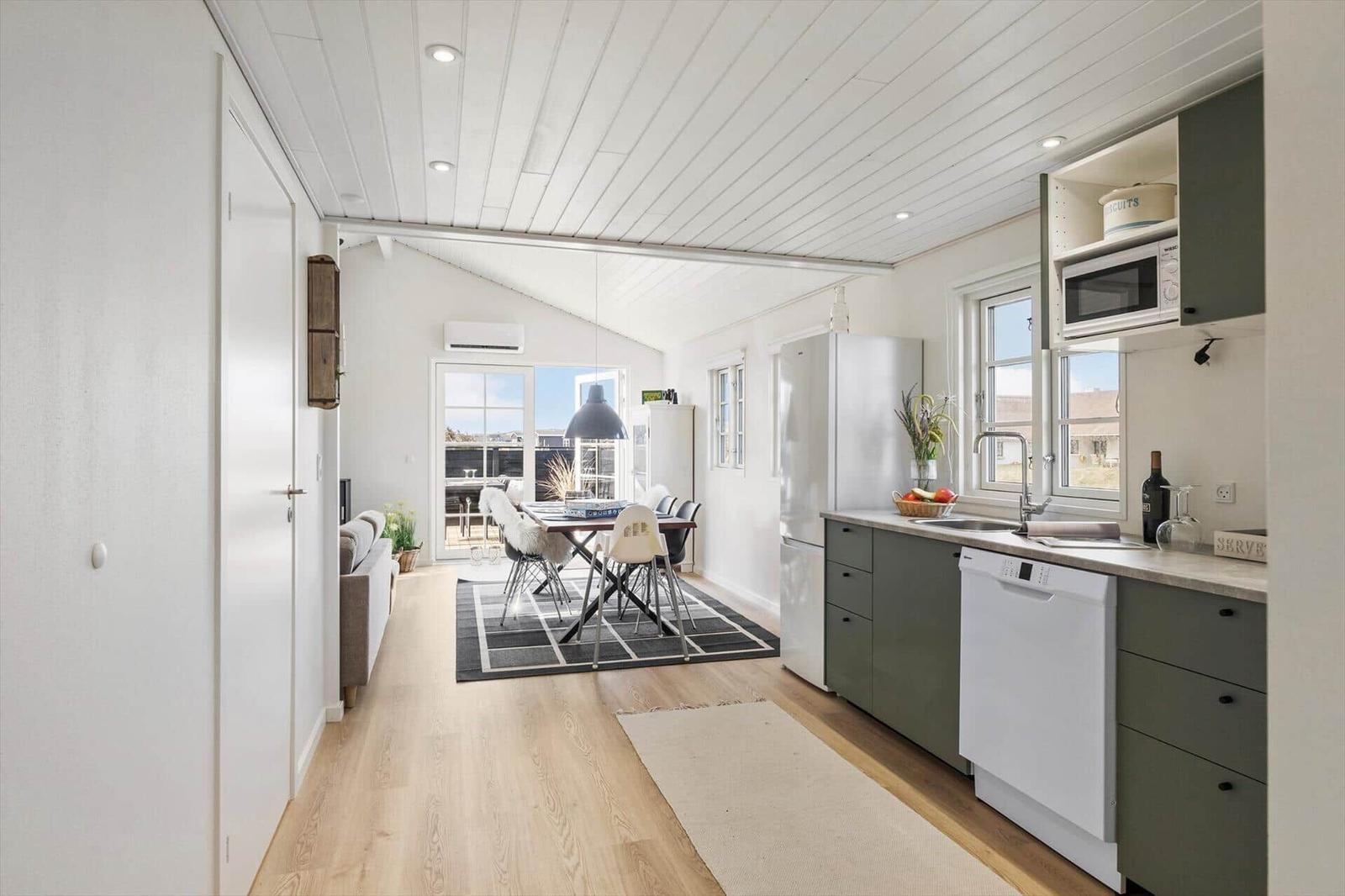 Küche mit grünen Schränken und weißer Spüle. Essbereich mit Tisch und Stühlen. Wohnbereich mit Sofa und Balkon.