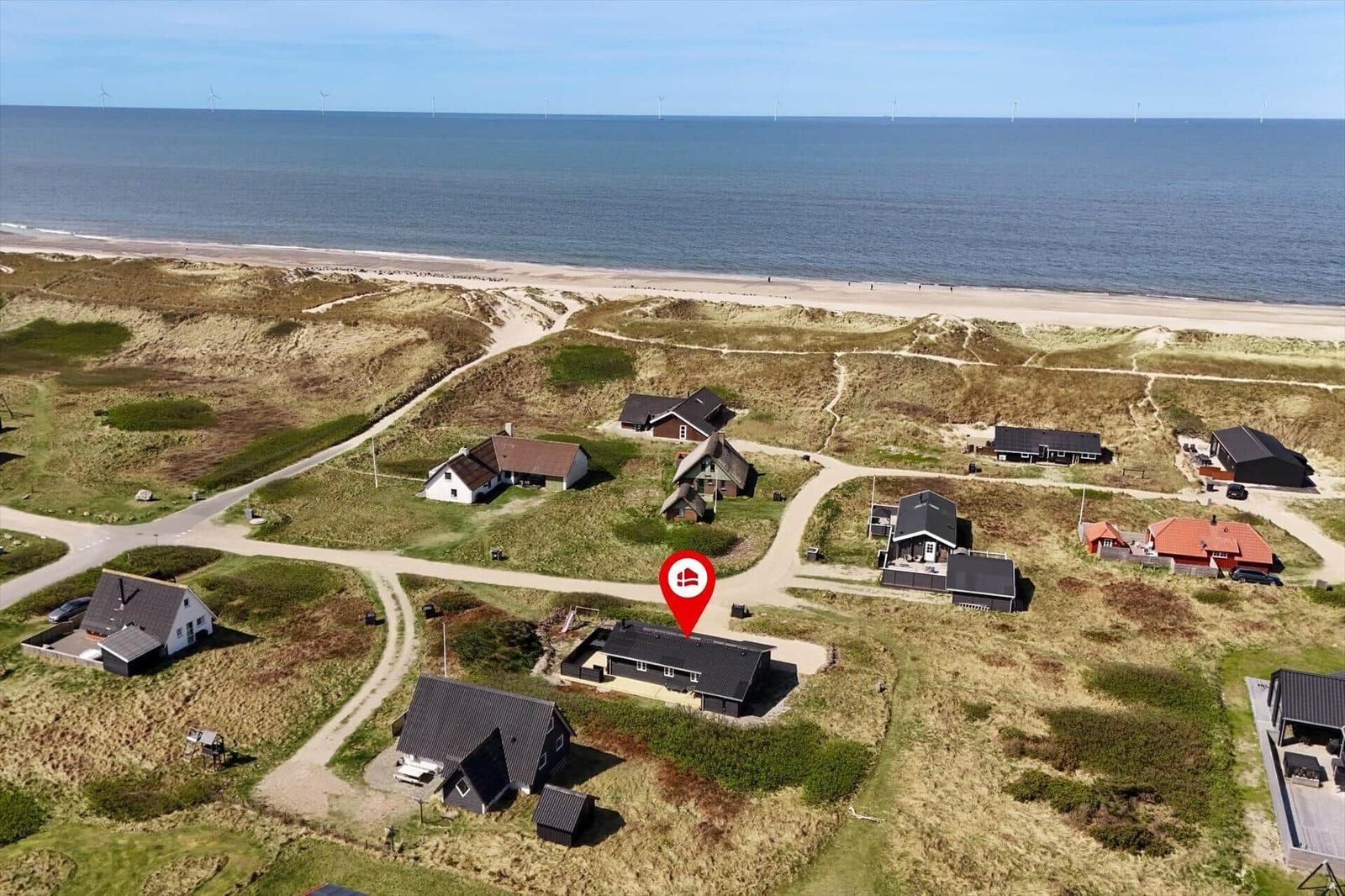 Haus mit Blick auf Strand und Dünen. Windräder sind im Hintergrund sichtbar.