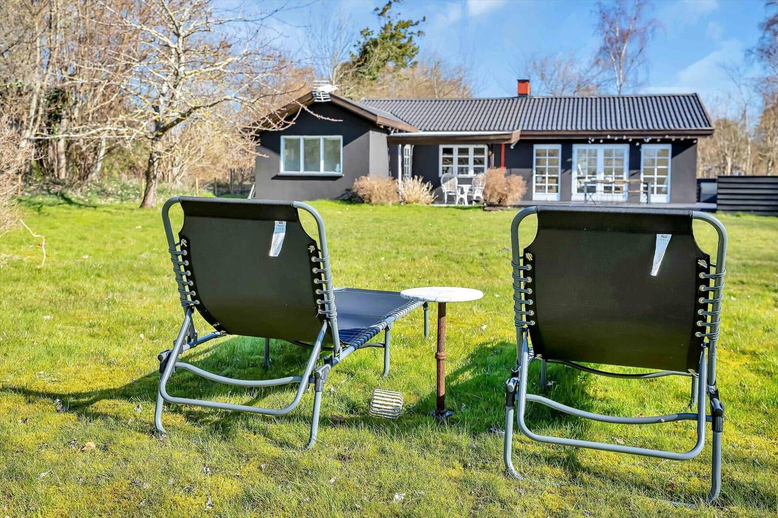 Zwei Liegestühle und ein Tisch auf einer grünen Wiese vor einem Haus.