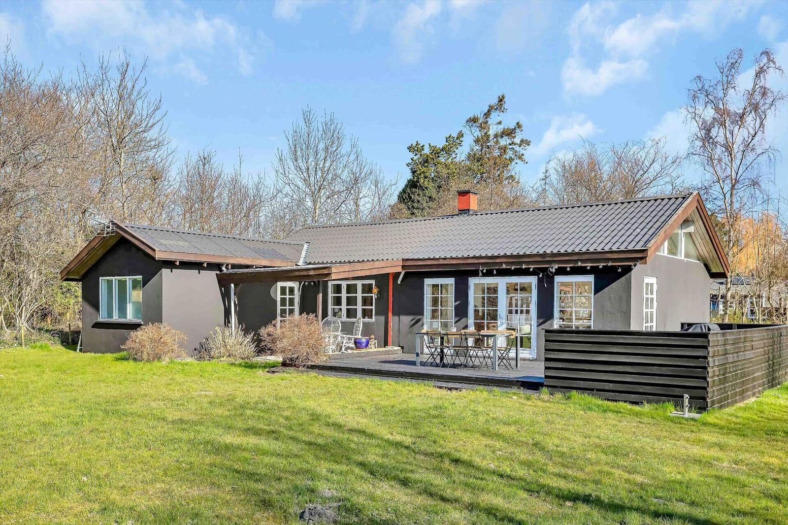 Ein Haus mit Terrasse und Garten. Es hat weiße Fenster und einen dunklen Anstrich.