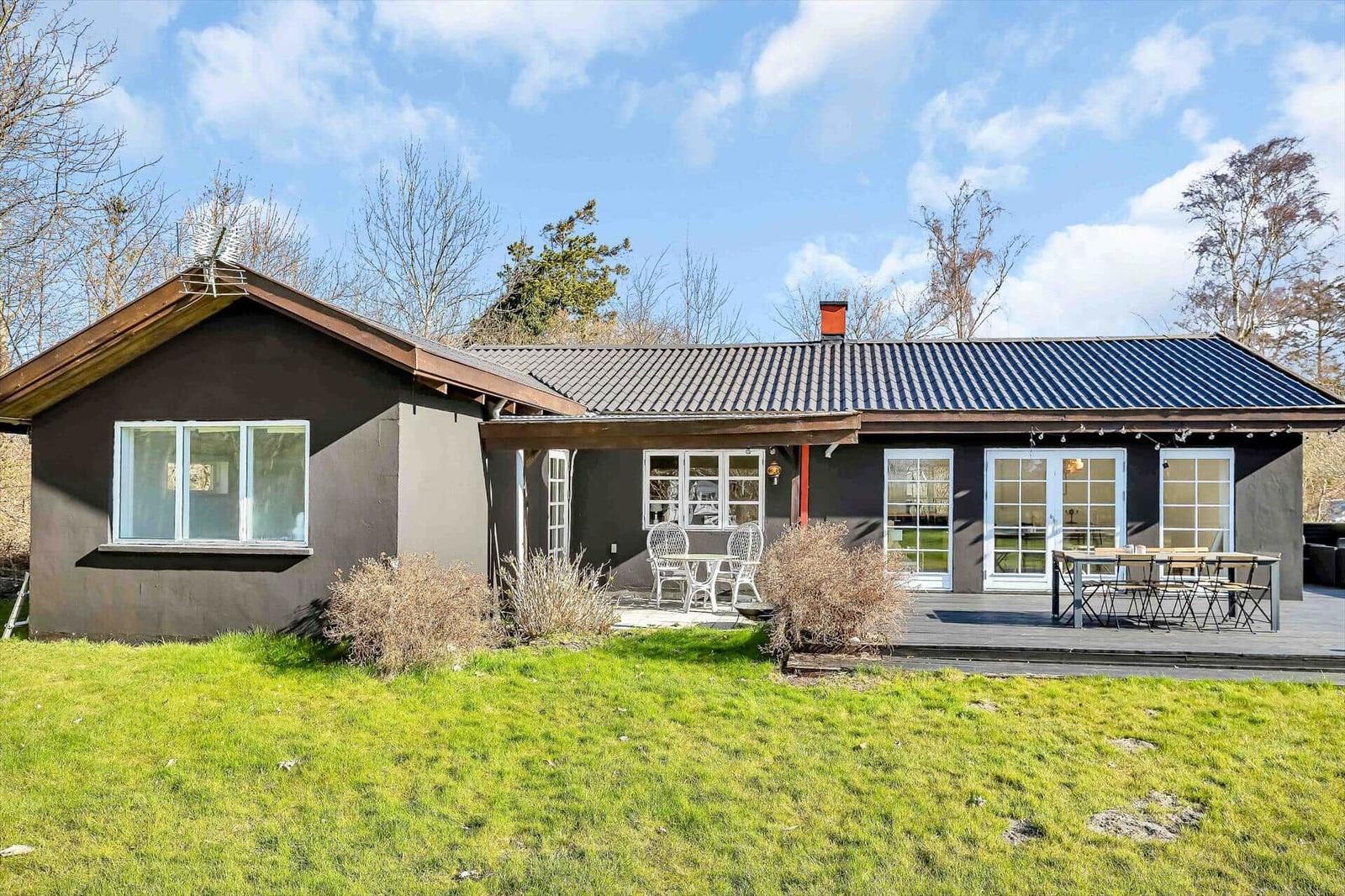 Ein dunkel gestrichenes Haus mit Terrasse und Garten. Weiße Fenster und Türen.