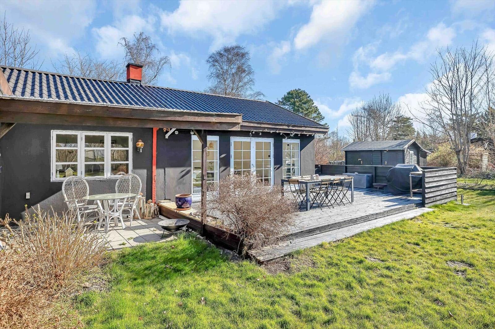 Ein Haus mit Terrasse, Garten und Grillplatz. Weiße Fenster und Türen.