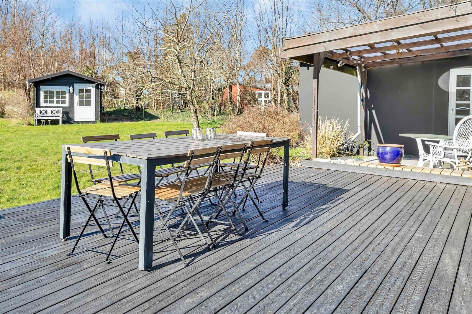 Terrasse mit Tisch und Stühlen, Pergola und Gartenhaus im Hintergrund.