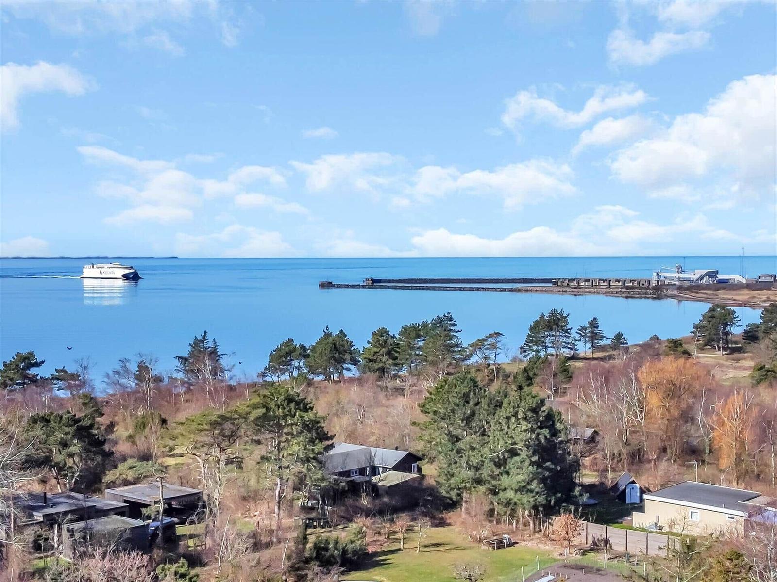 Meerblick mit Fähre und Hafen, umgeben von Bäumen und Häusern.