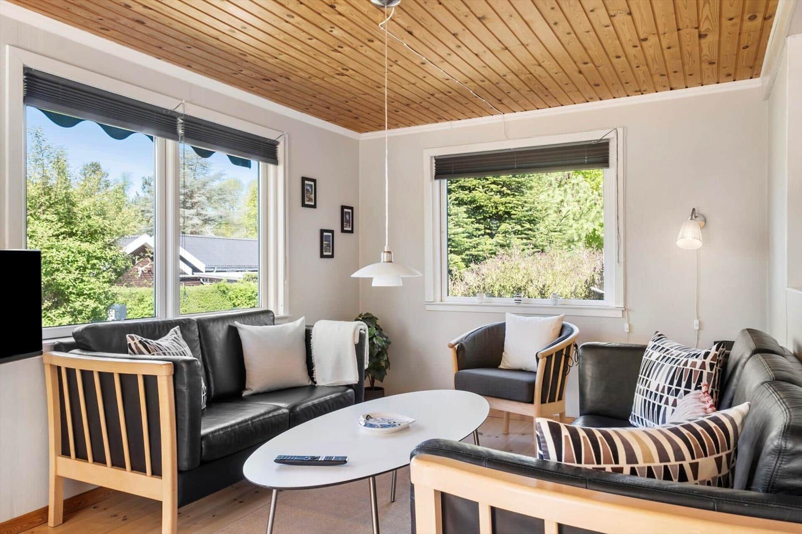 Living room with leather sofa, wooden ceiling, and view of green trees.