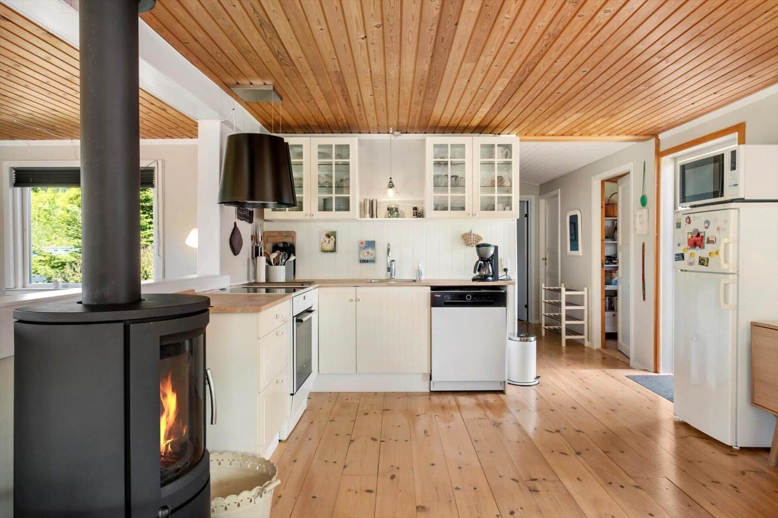 Kitchen with wooden floor, white cabinets, and wood-burning stove. View of garden through window.